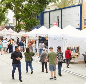 People walking through an outdoor street fair with white tent canopies